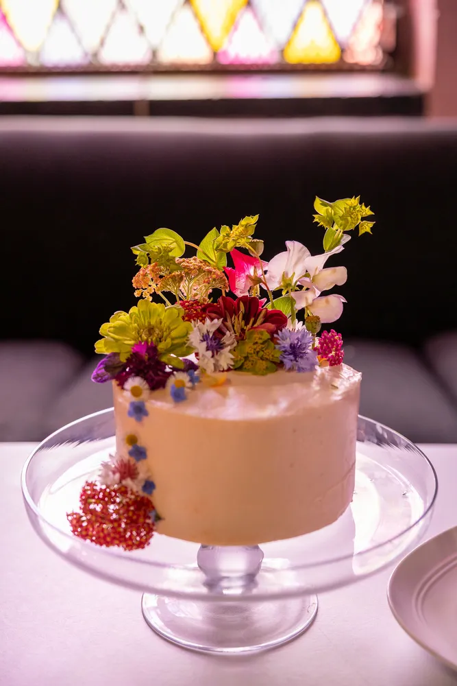 Small, frosted cake with delicate flowers arranged on top, displayed on a clear cake stand.