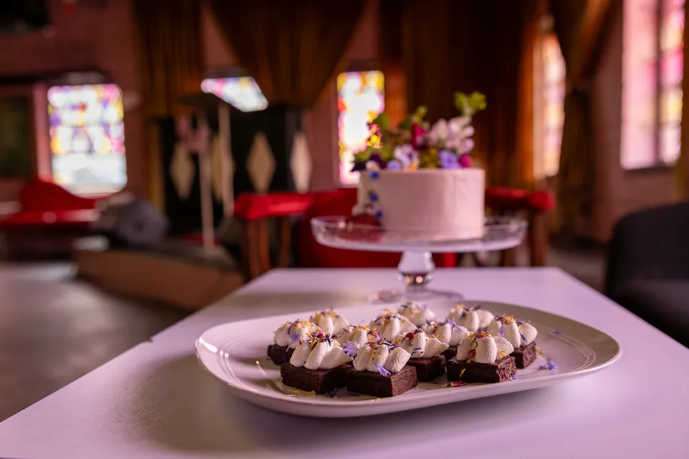 Brownie bites topped with cream and flowers on a white plate. Dessert treats for a celebration.