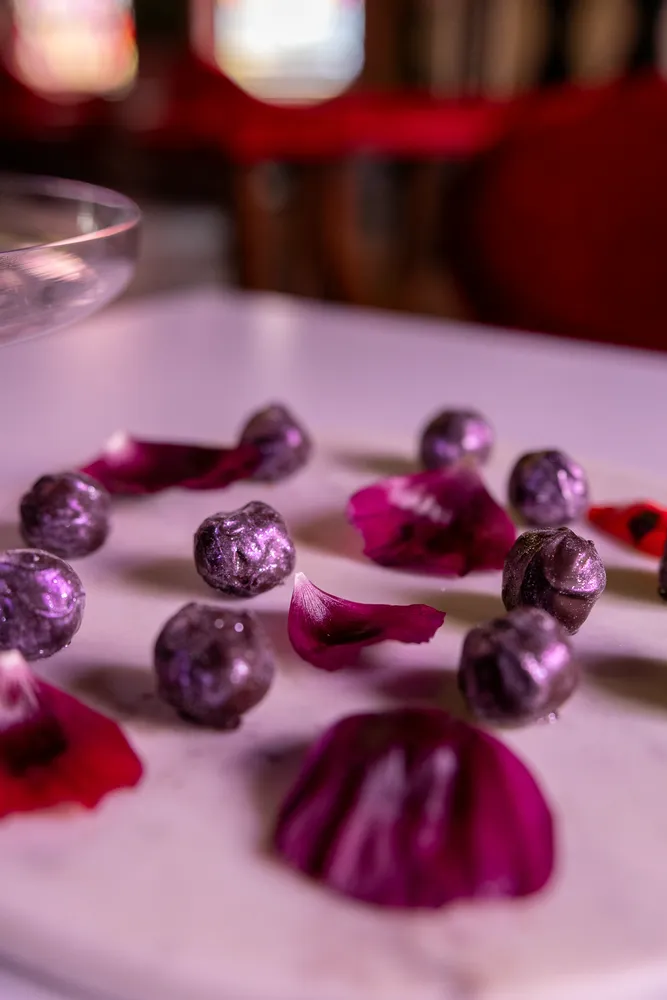 Close-up of violet macarons with rose petals on a white plate, creating a delicate and floral dessert presentation.