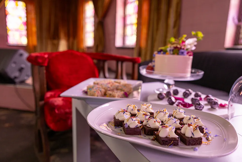 Mini chocolate cakes with whipped cream and edible flowers on a white platter, displayed for a dessert table.