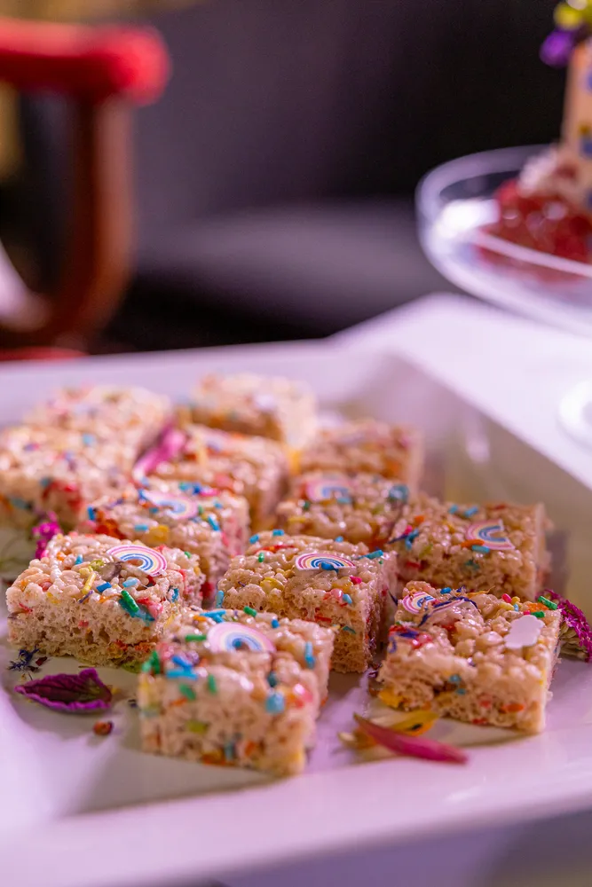 Colorful rice crispy treats arranged on a plate, dusted with sprinkles, and served with a side of fruit.