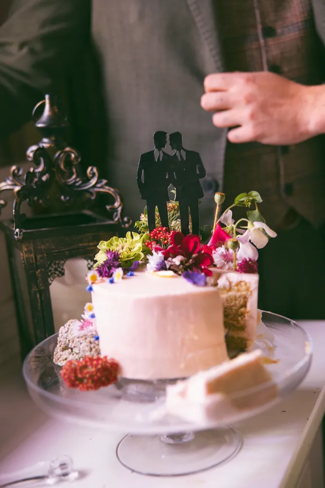 Close-up of a tiered wedding cake decorated with fresh flowers on a cake stand.