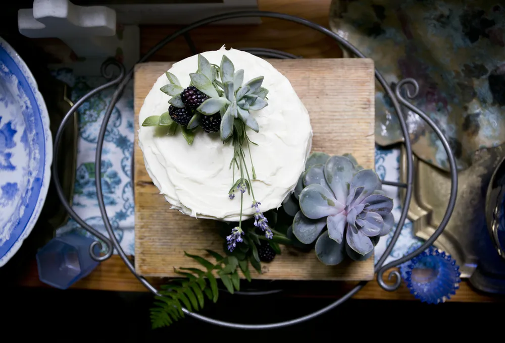 Small vanilla cake decorated with blackberries, lavender, and succulents on a wooden board.