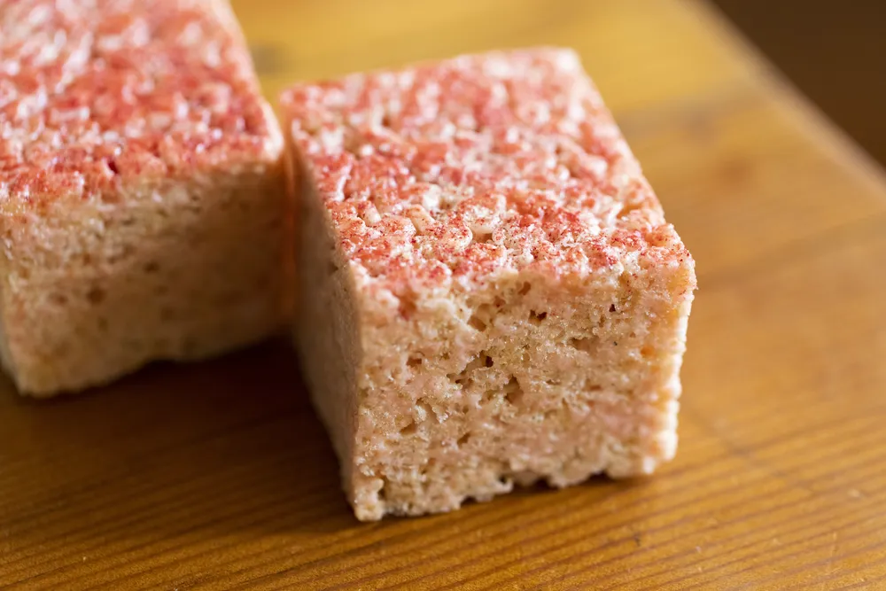 Close-up of a strawberry shortcake square with a crumbly texture and pink frosting.
