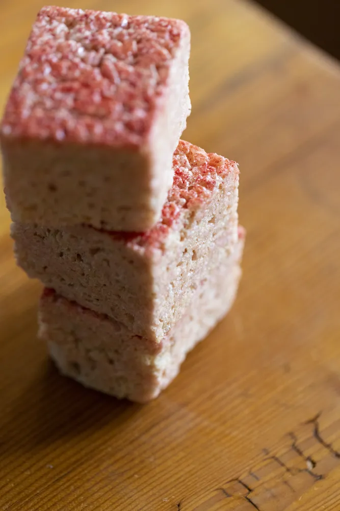 Fluffy pink marshmallows stacked on a wooden surface, showcasing a close-up view of their soft texture.