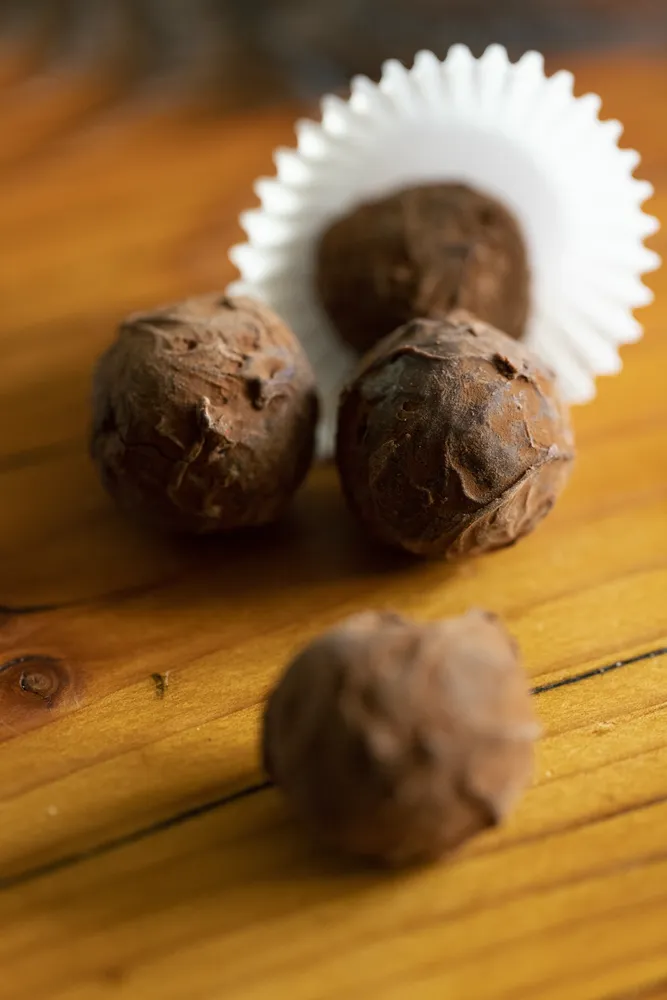 Close-up of three chocolate truffles on a wooden surface, showcasing their rich color and smooth texture.