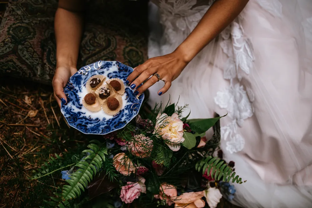 Blue ceramic plate with meringue cookies rests on a floral bed, held by a hand with blue nail polish.