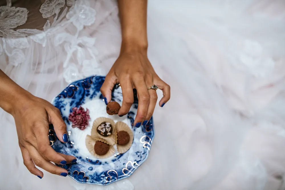 Hands holding a blue ceramic dish with truffles and edible flowers.