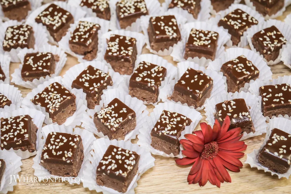 Assorted mochi donuts with sesame seeds arranged on a platter, garnished with a red flower.