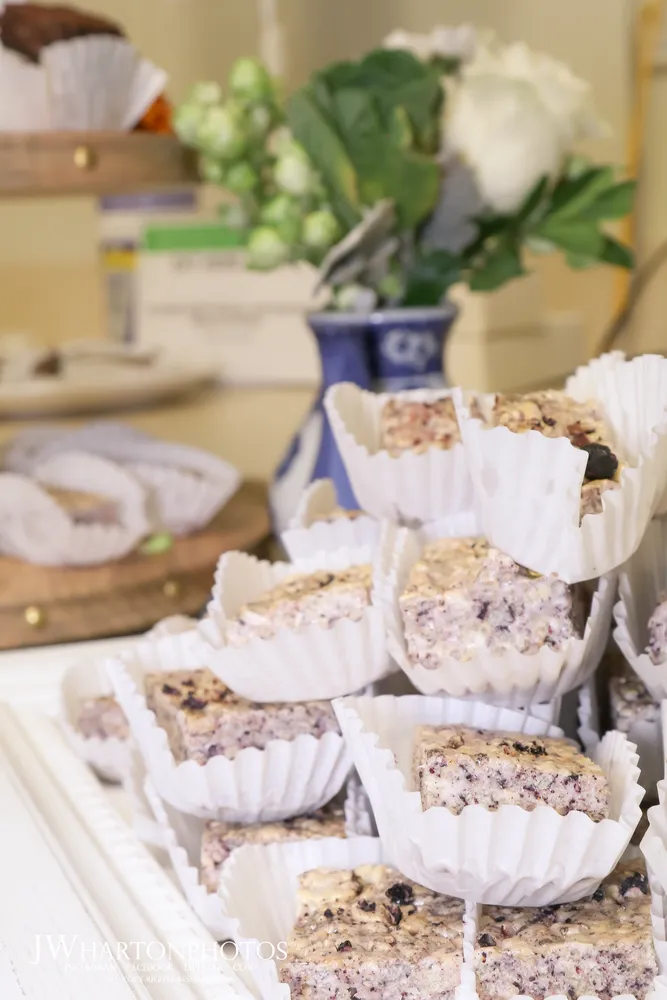 Blueberry muffins in white paper liners sit on a wooden surface, dusted with powdered sugar.