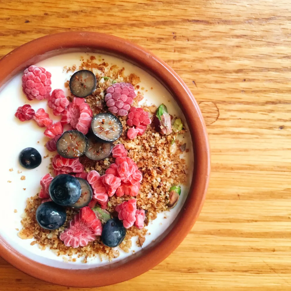 Yogurt parfait with fresh raspberries, blueberries, and granola in a glass bowl, viewed from above.