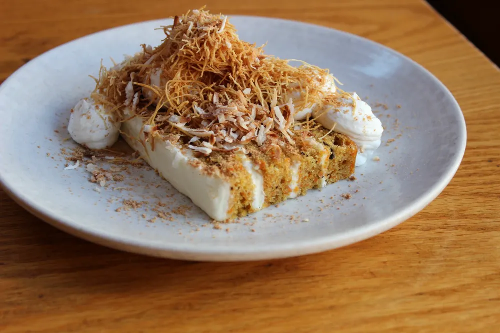 Coconut cream pie slice with whipped cream and toasted coconut flakes on a white plate.