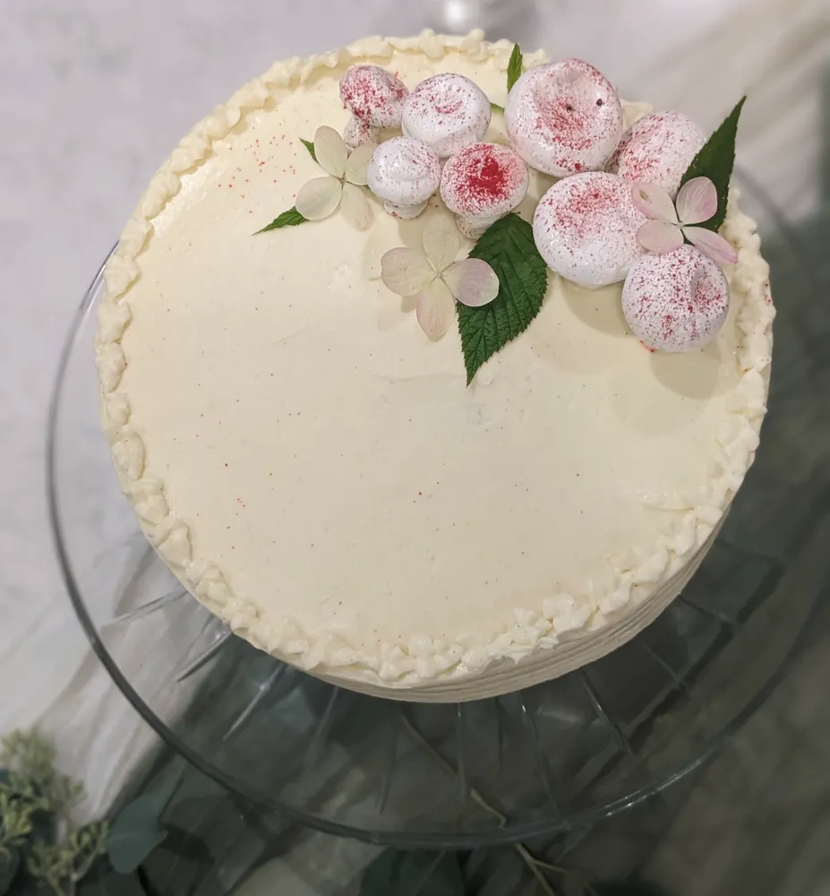 Vanilla cake with white frosting and pink flower accents on a cake stand.