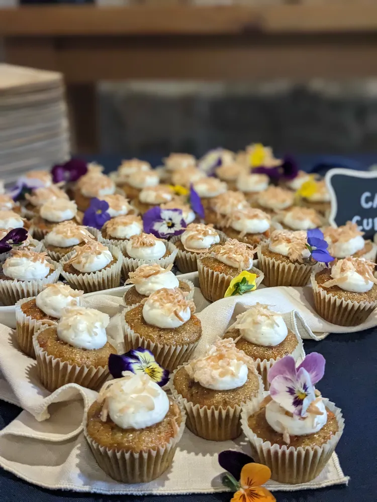 Assorted cupcakes with white frosting and edible flower garnishes displayed on a table.
