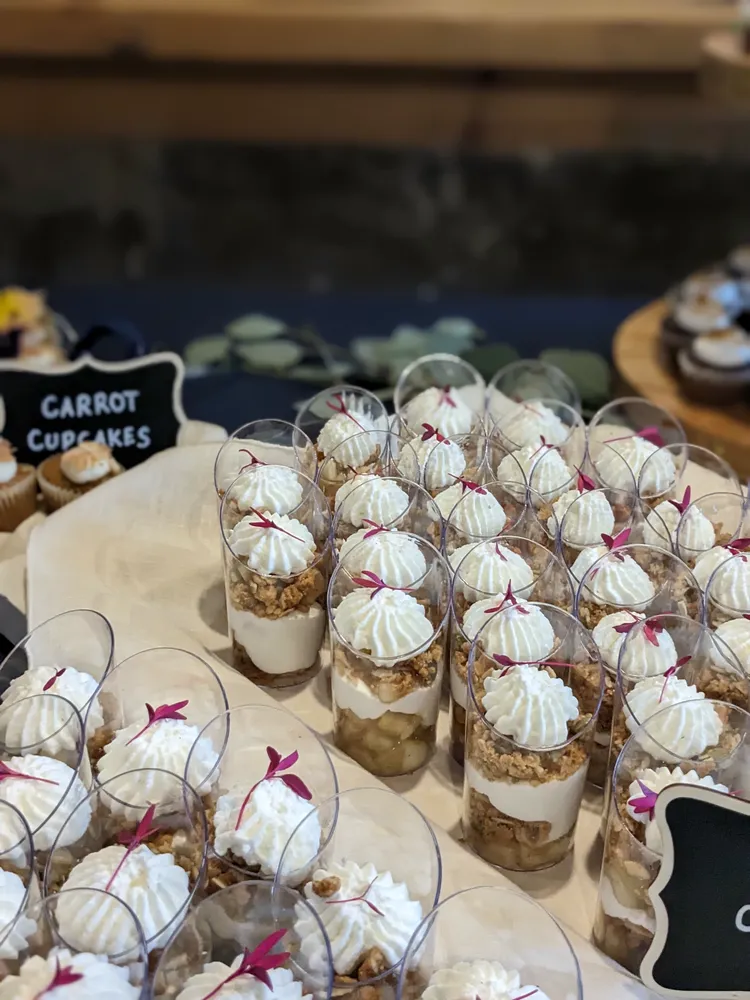 Mini trifle desserts in clear cups with whipped cream and cherry topping, arranged on a dessert table.