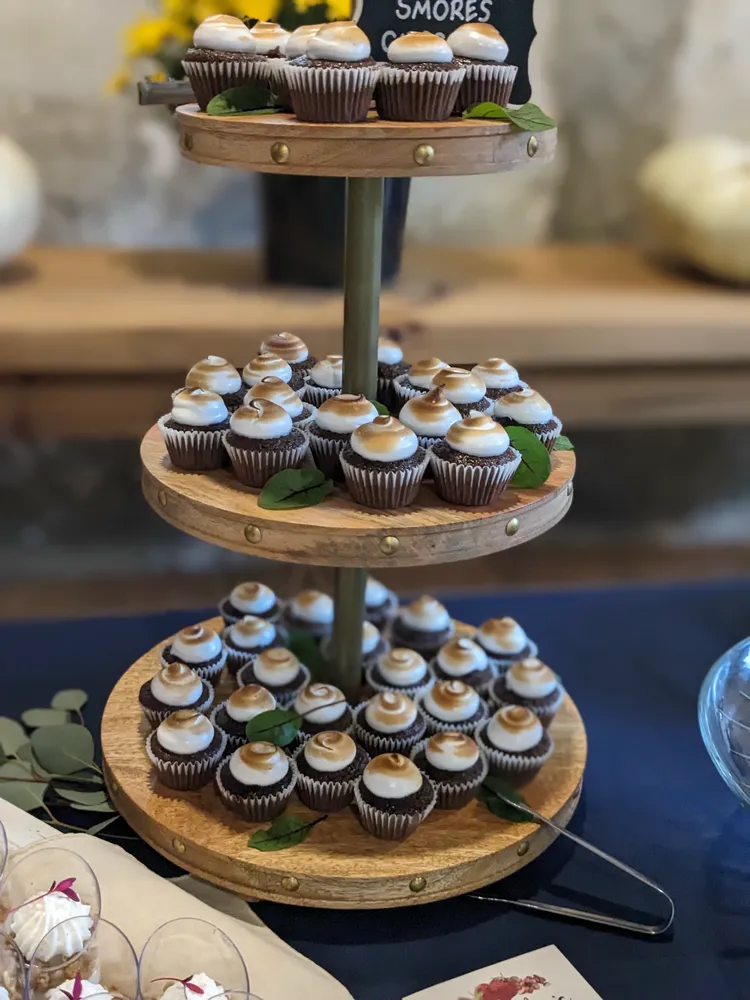Mini cupcakes arranged on a wooden tiered stand. The cupcakes have vanilla frosting and chocolate sprinkles.