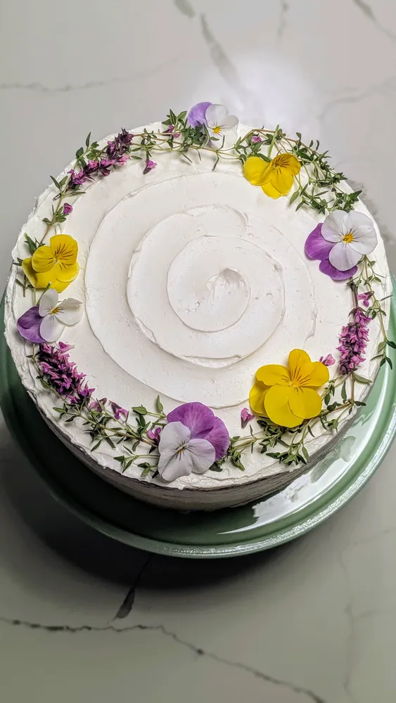 Vanilla cake with buttercream frosting and fresh thyme and pansy flowers arranged on top.