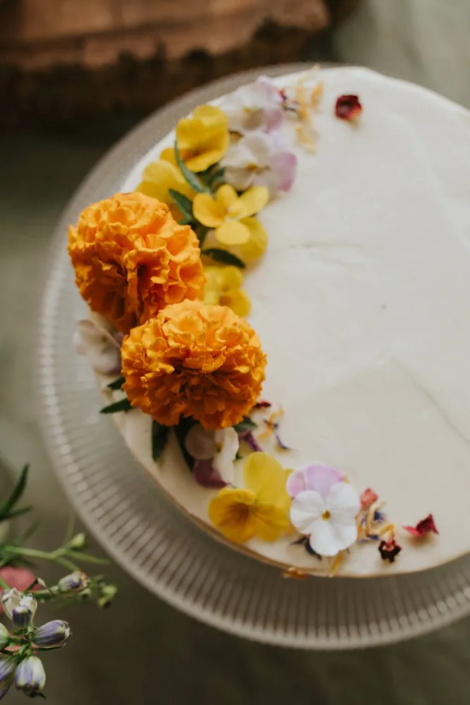 Close-up of a vanilla cake decorated with vibrant orange and yellow flower petals on a white plate.