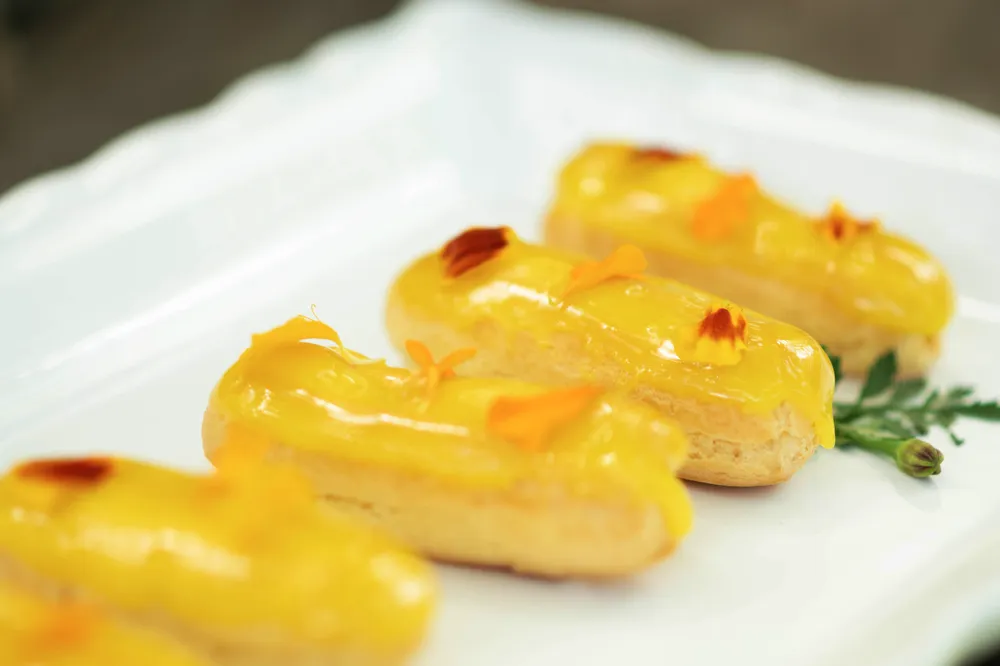 Golden-brown cream puffs dusted with powdered sugar, arranged on a white plate with fresh herbs.