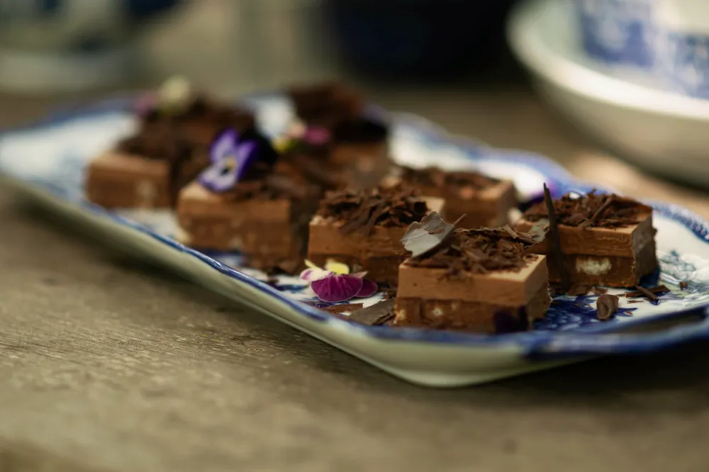 Chocolate truffles arranged on a blue and white patterned plate, garnished with chocolate shavings and delicate pink flowers.