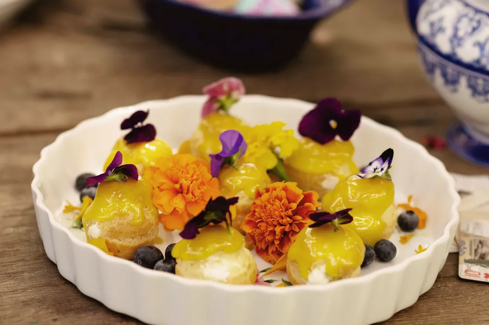 Lemon mousse dessert with blueberry garnish and edible flower petals arranged in a white ramekin.
